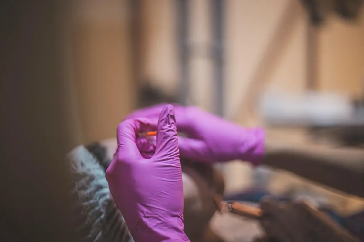 Profissional com luvas rosa segurando uma seringa de procedimento estético