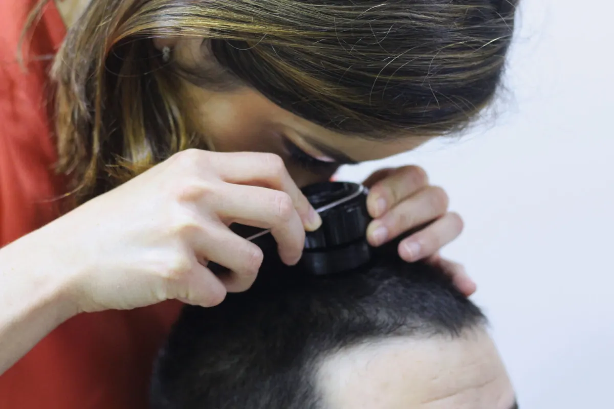 Dermatologista examinando o couro cabeludo de um paciente com dermatoscópio